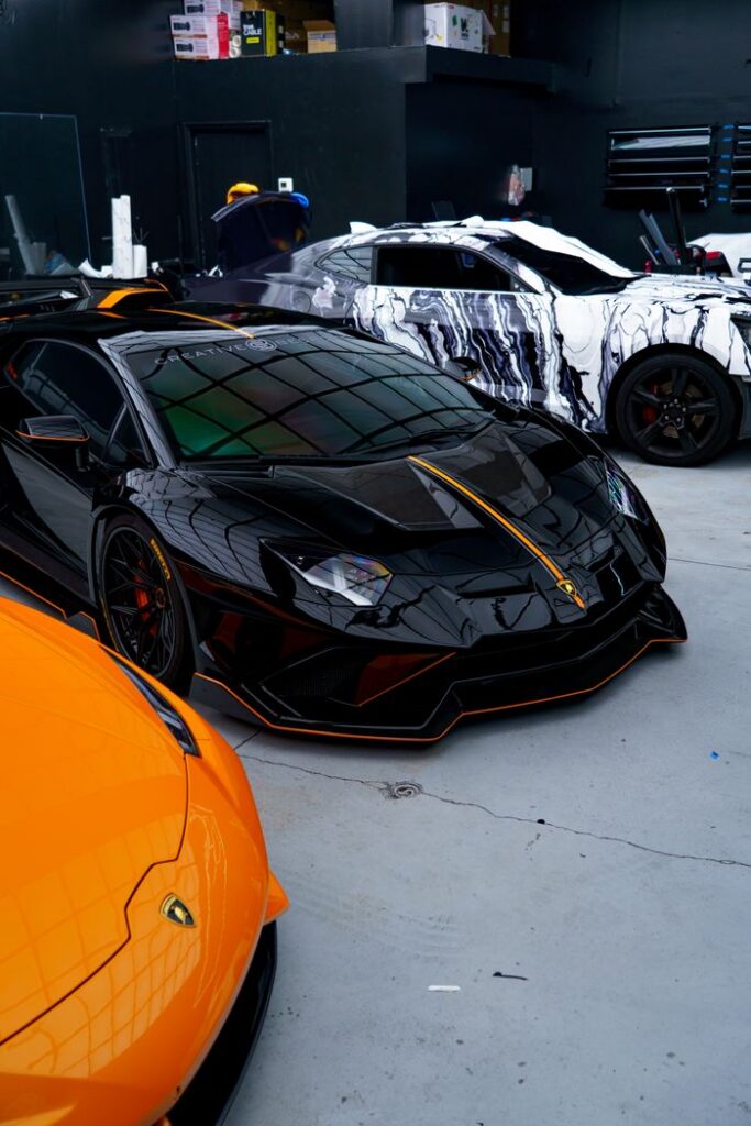 Black and orange luxury sports cars in a sleek, urban garage setting.