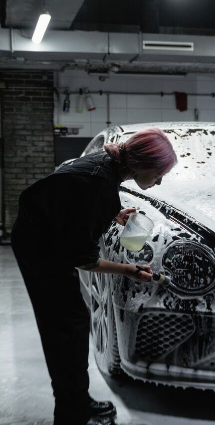 A worker professionally washing a luxury car in a modern garage filled with foam.